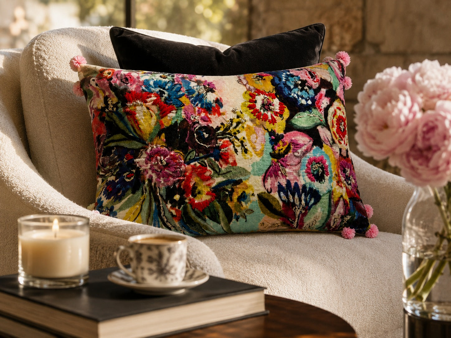 Wildflower Riot Cushion styled on a cream armchair beside pink peonies