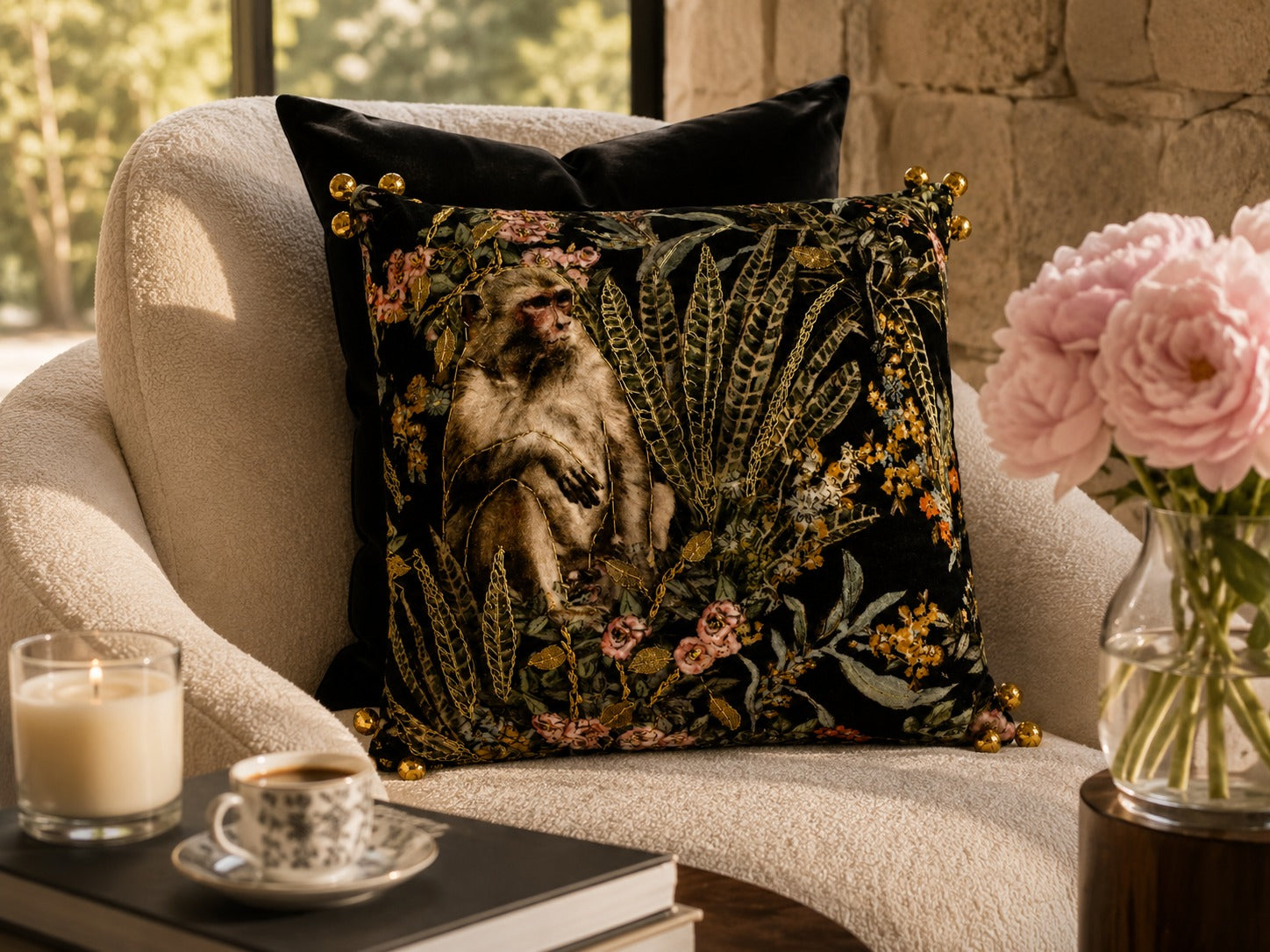 Macaque Botanical Cushion styled on a cream armchair beside pink peonies